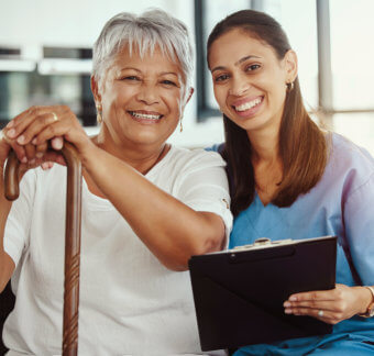 elder woman and female caregiver holding clipboard are smiling