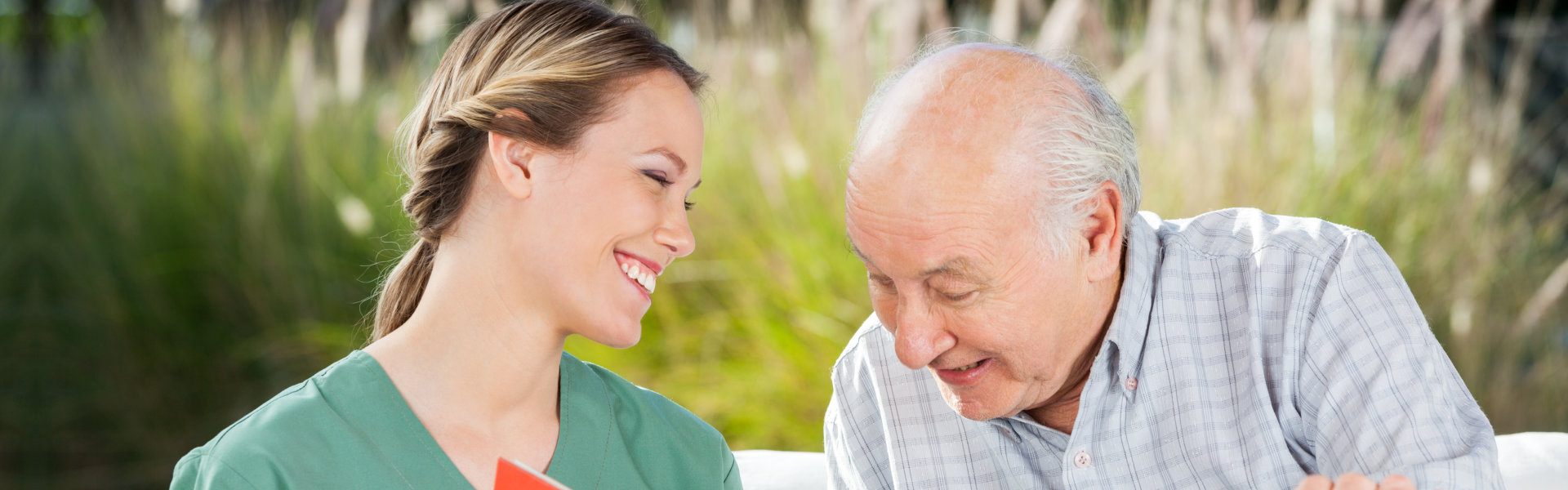 Smiling female nurse looking at senior man while reading book