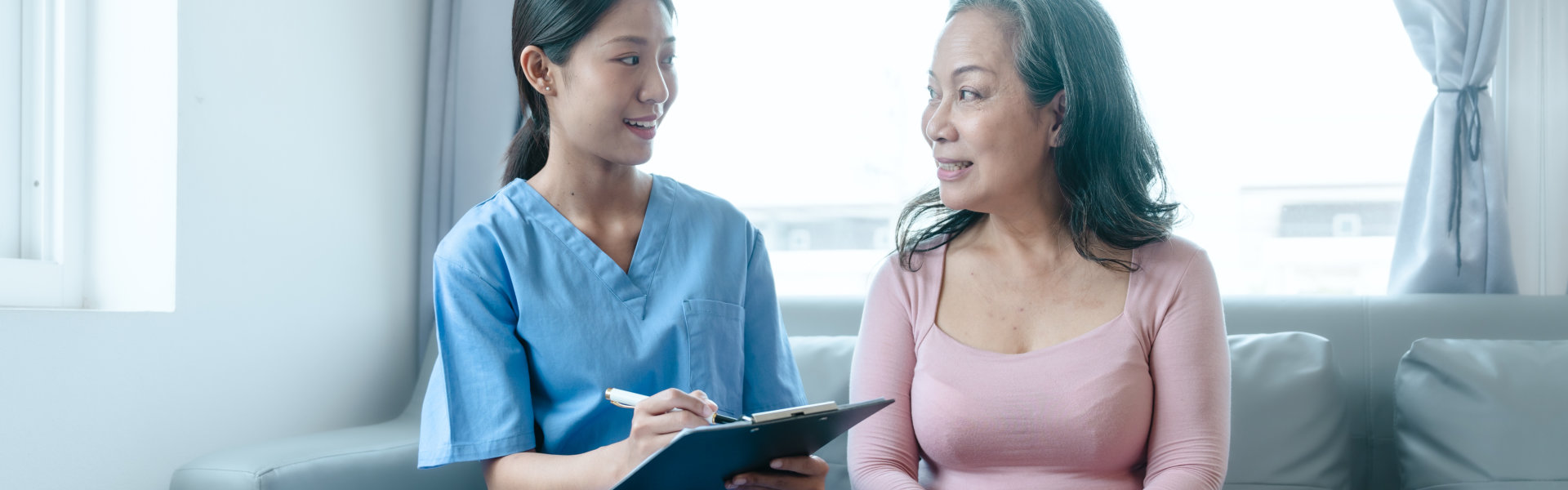 Female nurse holding a clipboard while talking to the elder woman