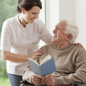 Elder man holding a book looking at the female caregiver